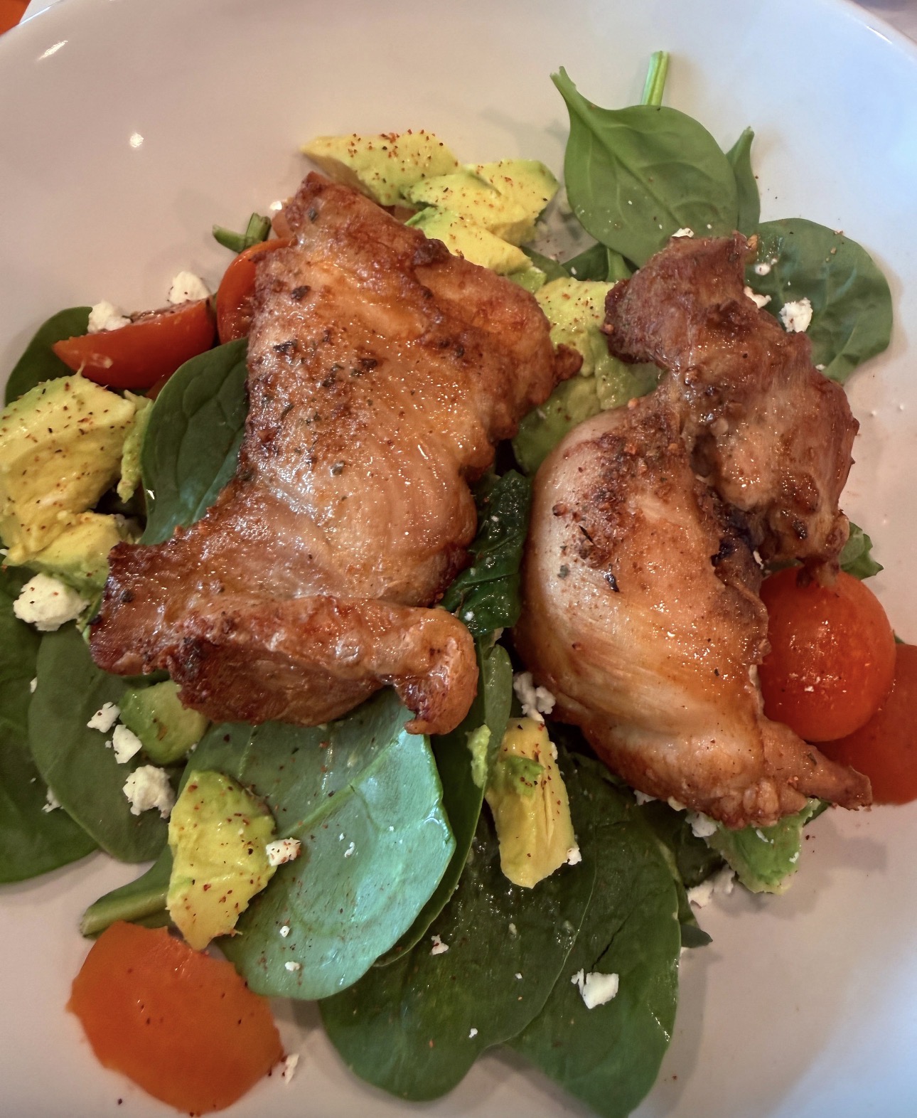 Pan-seared chicken thighs over spinach and avocado salad